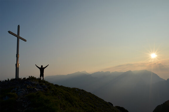 Wanderer am Gipfelkreuz im Rofangebirge bei Sonnenaufgang