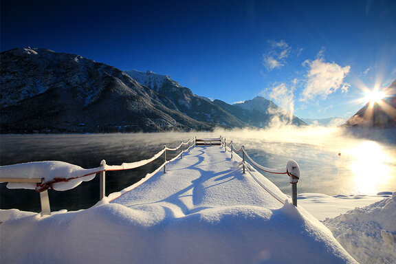 Verschneiter Steg am Achensee bei Sonnenaufgang im Winter